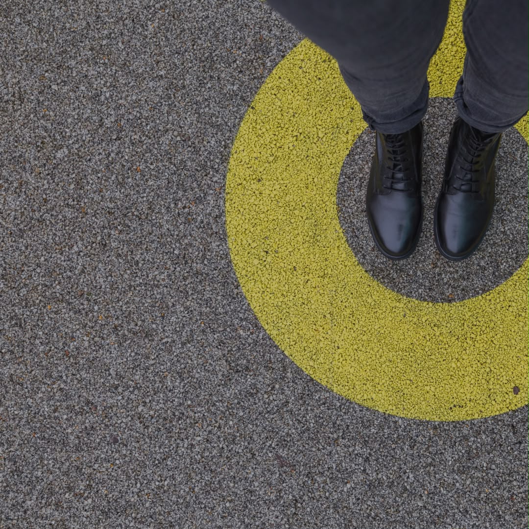 Schwarze Schuhe stehen in einem gelben Kreis auf grauem Asphalt